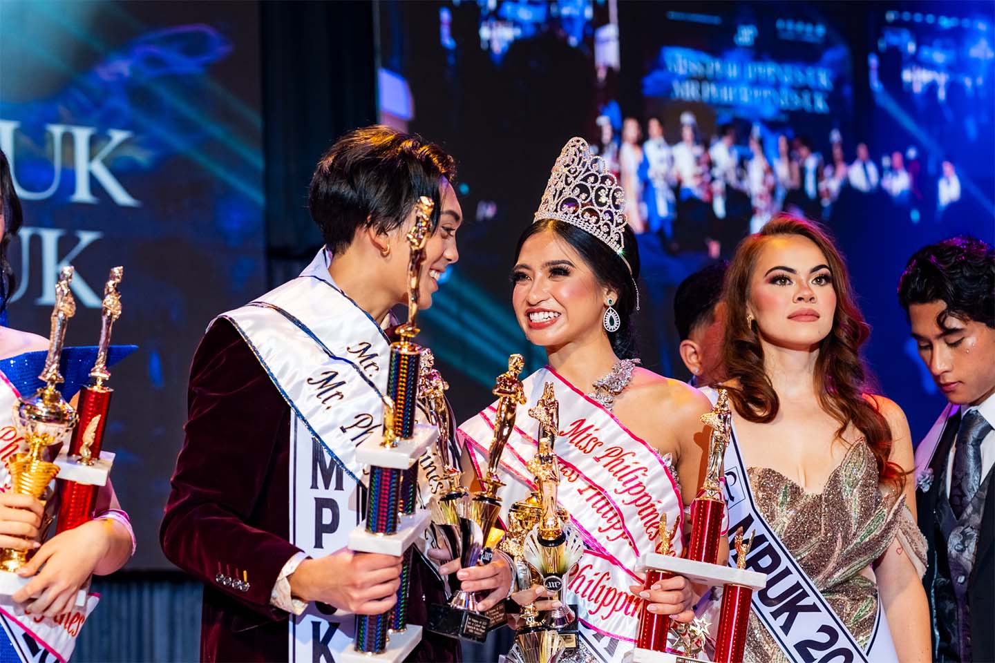 Miss & Mr. Philippines UK winners smiling together holding their trophies.